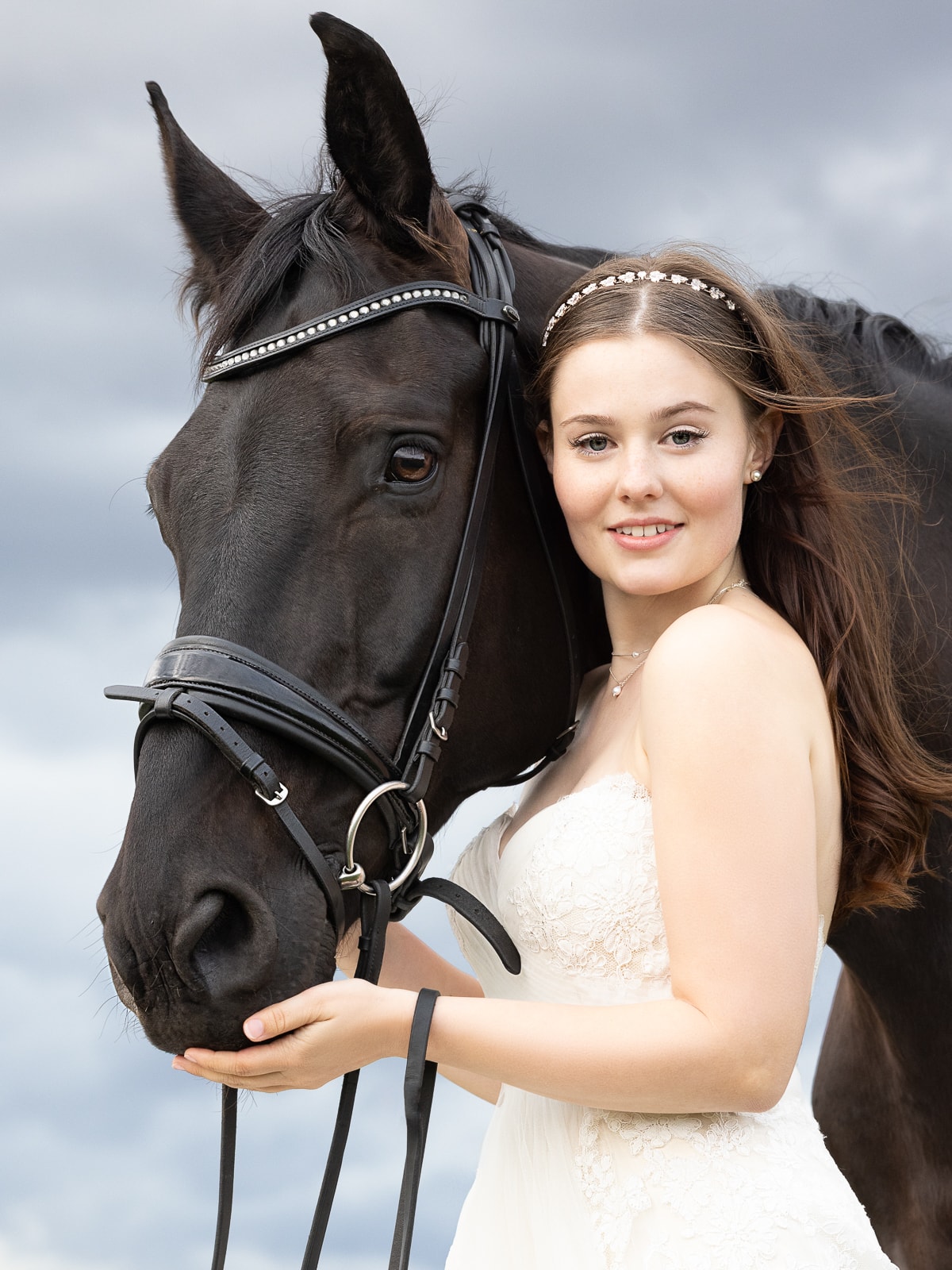 Young bride in white dress posing with dark horse