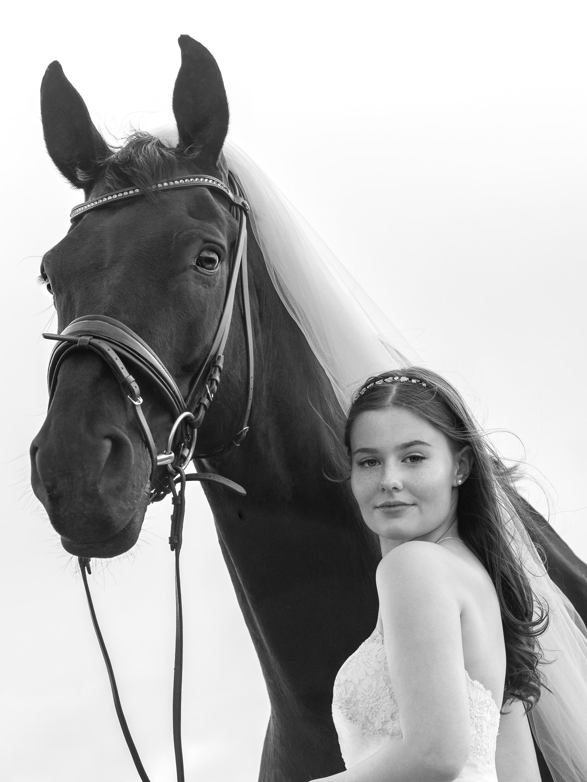 Bride in white dress gently touching dark horse