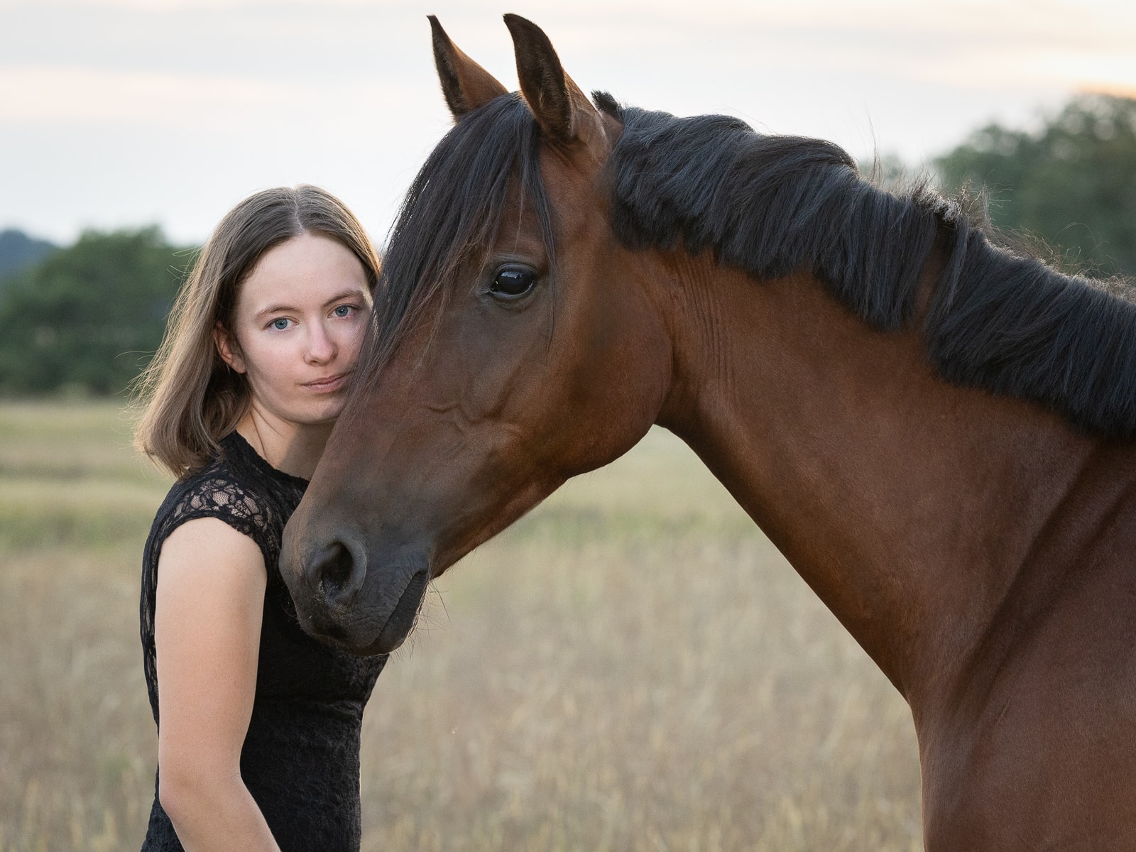 Woman and brown horse in tender touch on pasture