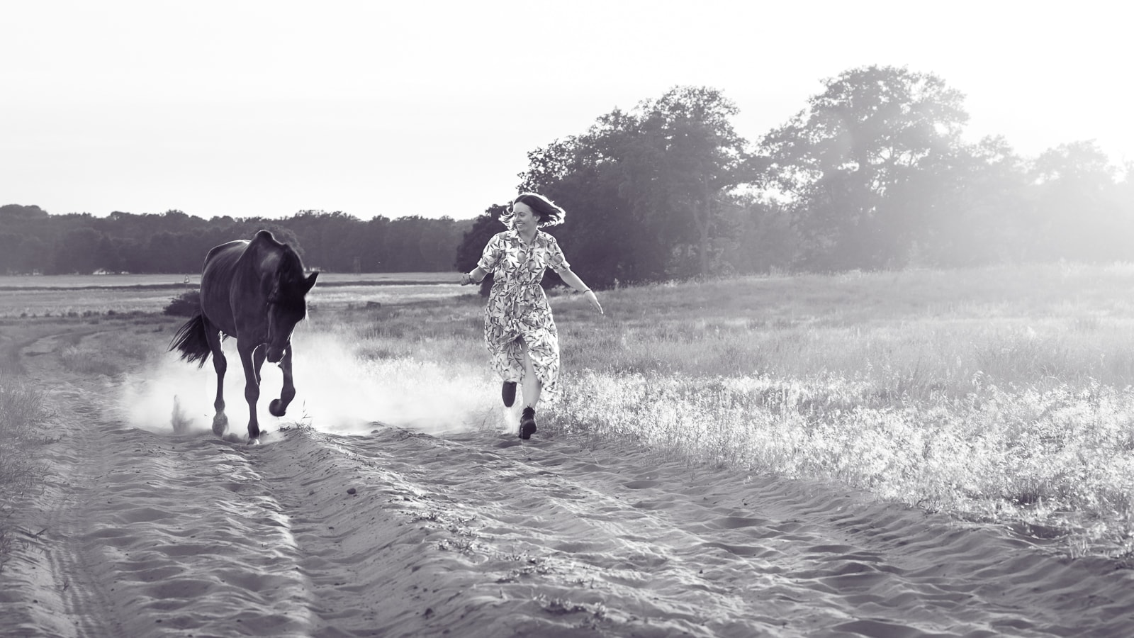 Woman and dark horse running dynamically through water in black and white