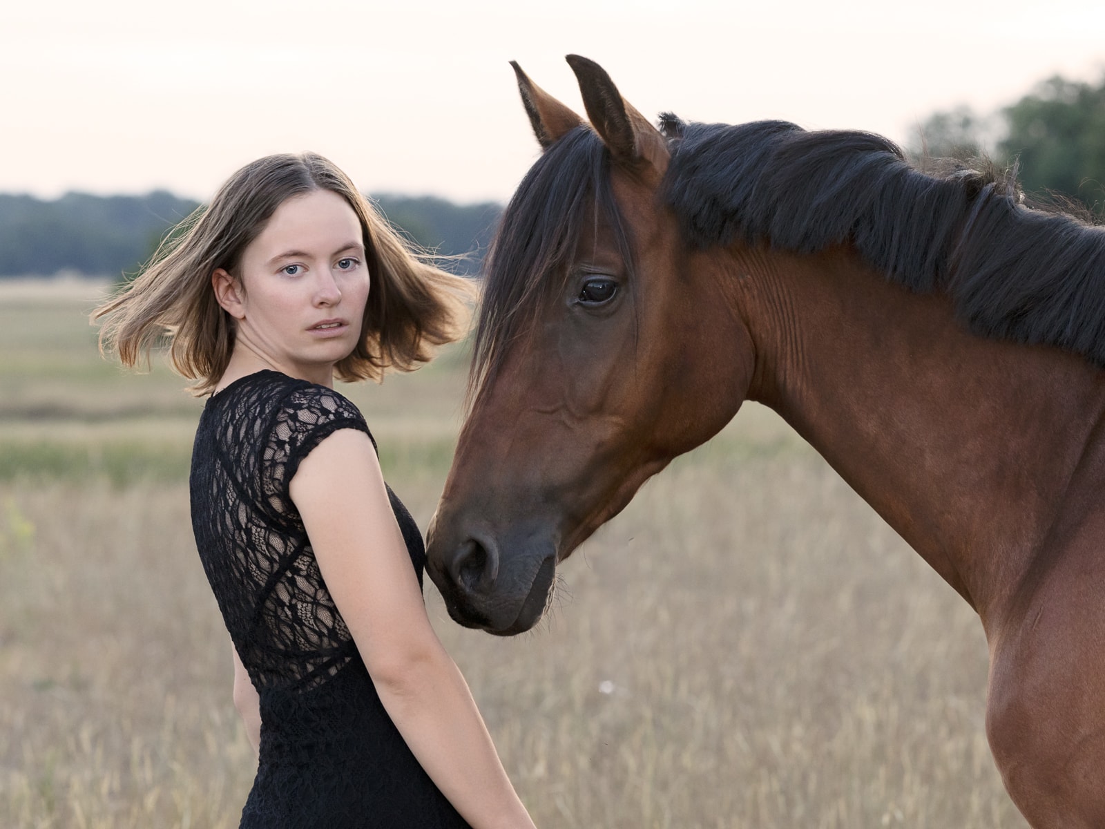 Woman in black dress lovingly greeting her brown horse on pasture